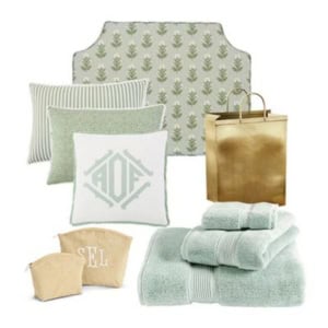 A collection of bedding and bath items including pillows, towels, a headboard, toiletry bags, and a gold gift bag, all in soft green, white, and gold tones.