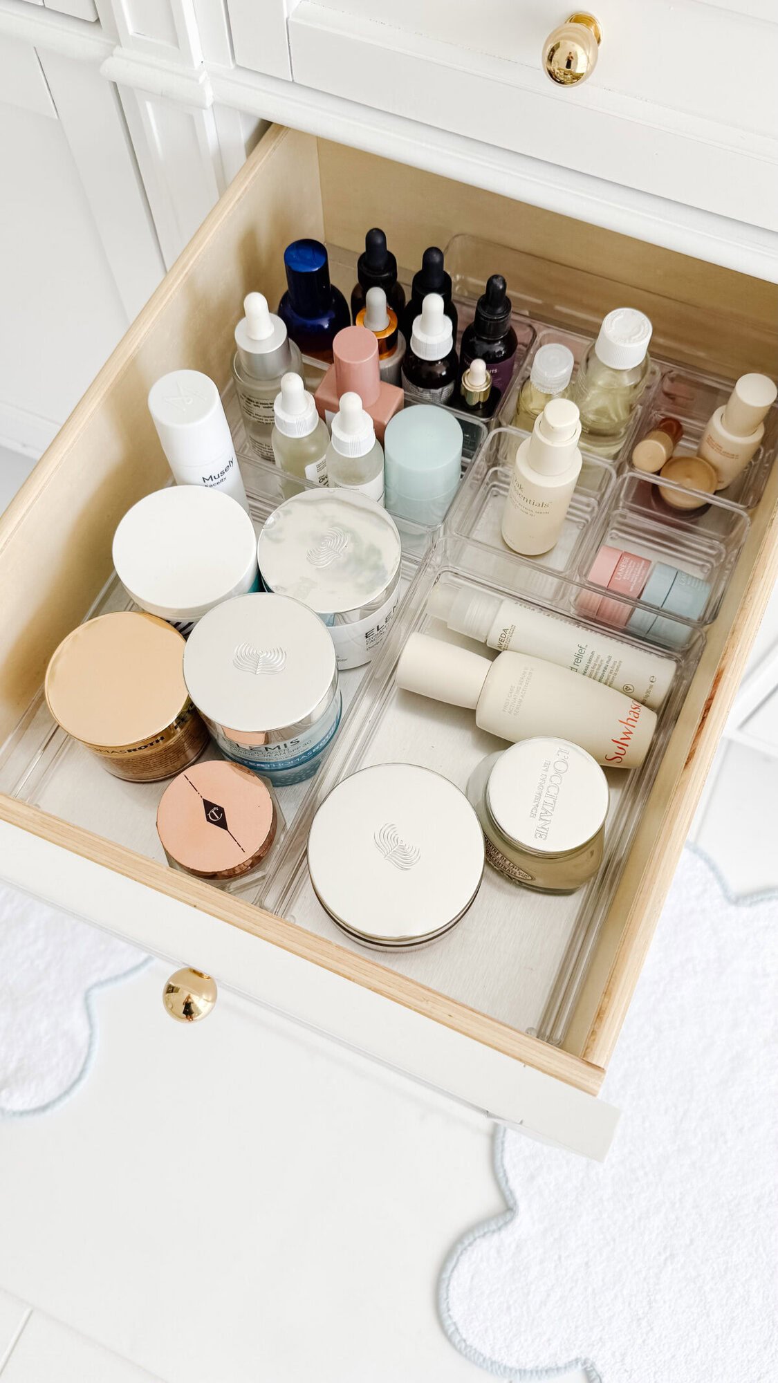 An organized drawer featuring various skincare and beauty products—creams, jars, dropper bottles, and tubes—all neatly arranged with clear plastic drawer organizers.