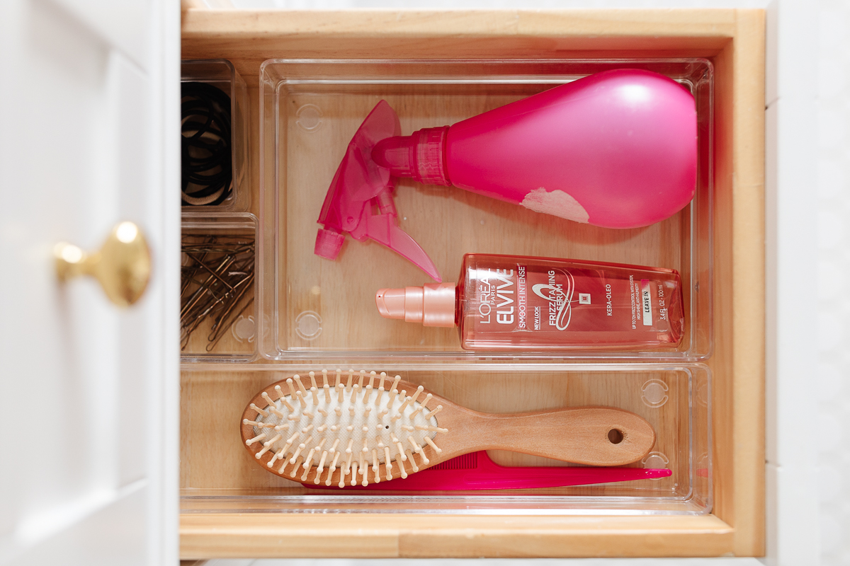 A drawer organizer with a pink hair brush and a bottle of hairspray.