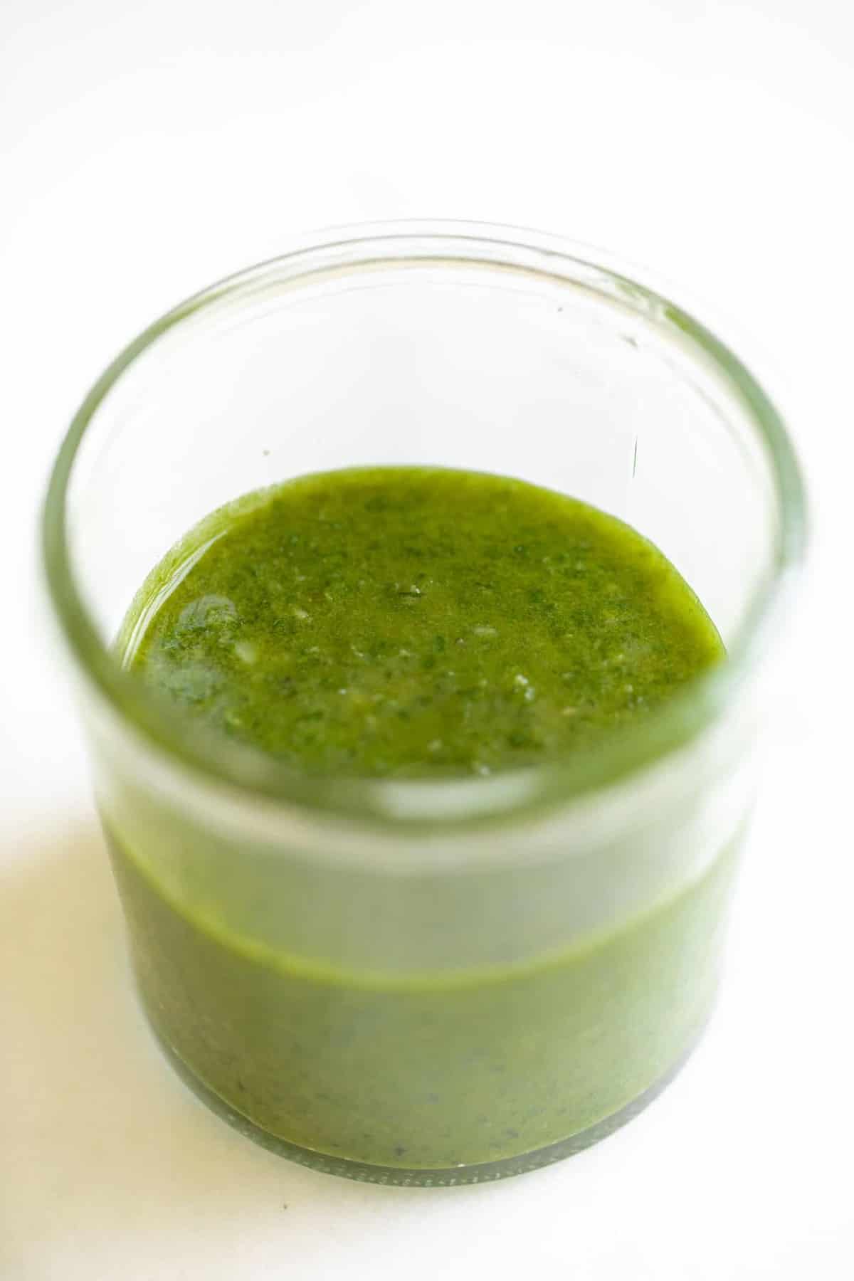 Marble surface with a small clear jar of homemade pesto recipe.