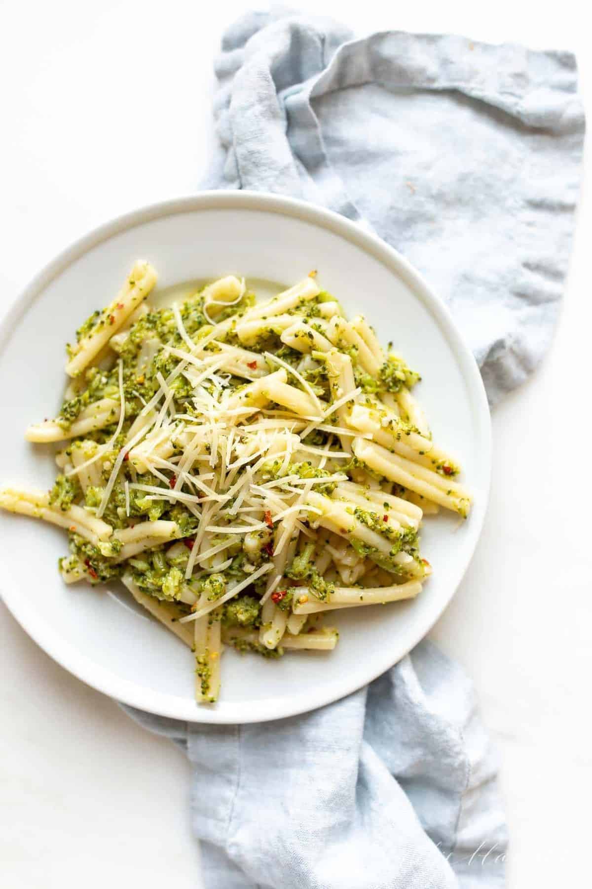 A white plate full of broccoli pasta, blue linen napkin behind