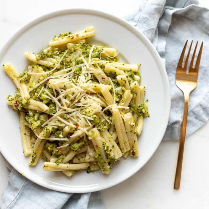 A white plate filled with broccoli pasta, blue napkin behind.