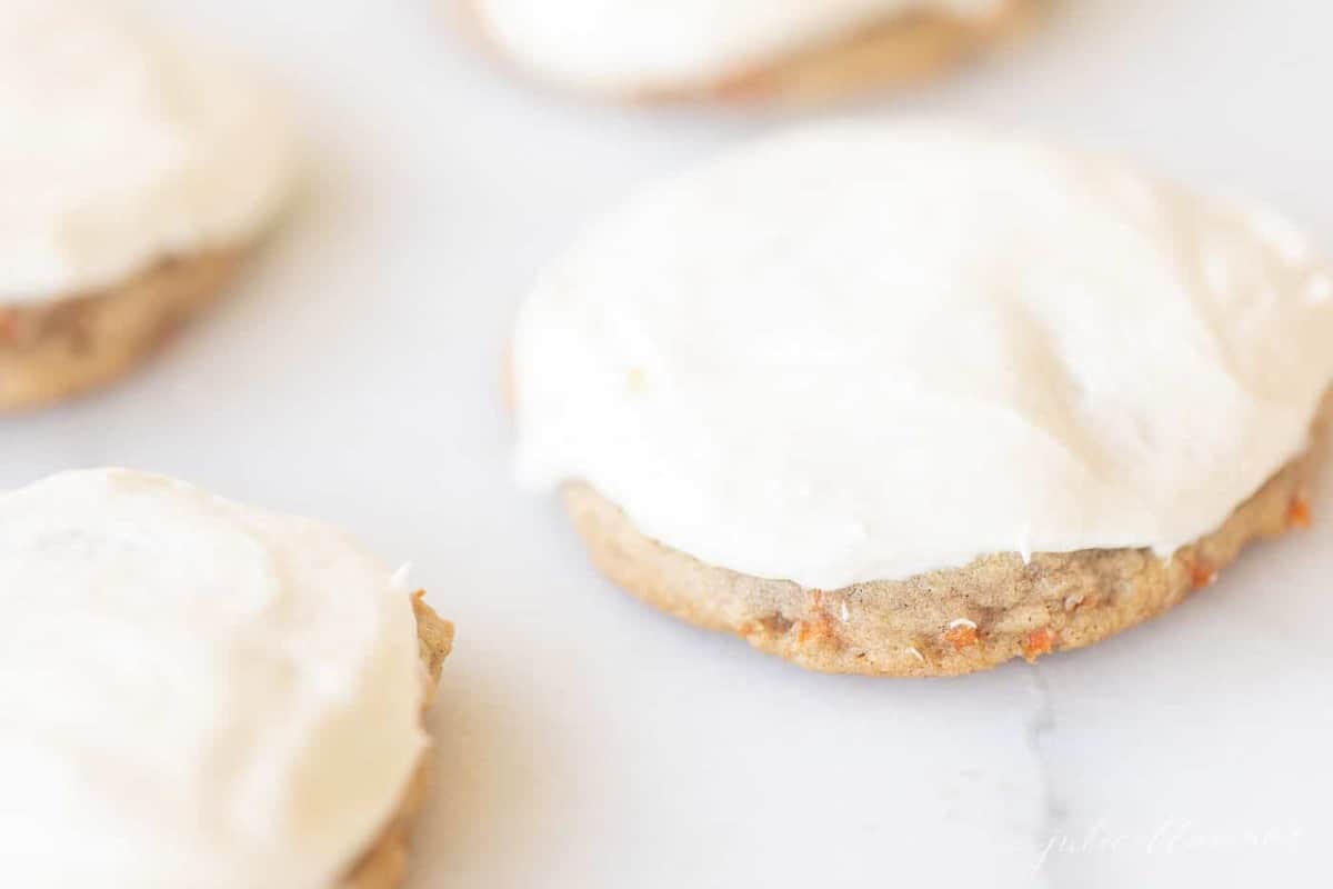 Carrot cake cookies frosted with cream cheese frosting on a marble surface.