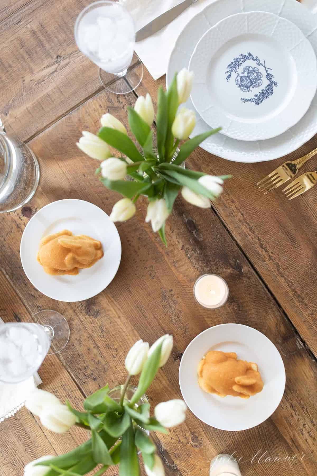 A wooden table filled with miniature Easter cakes and tulips for Easter Flowers