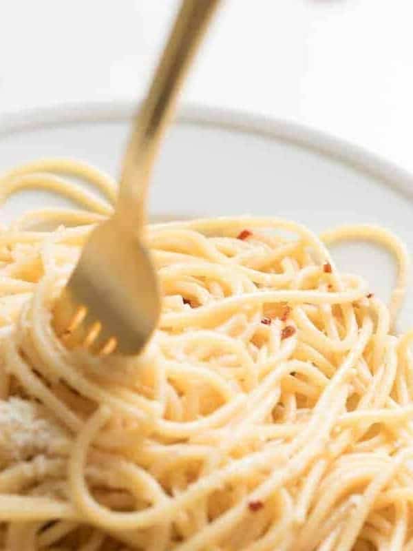 A white plate full of pasta with a gold fork sticking out.
