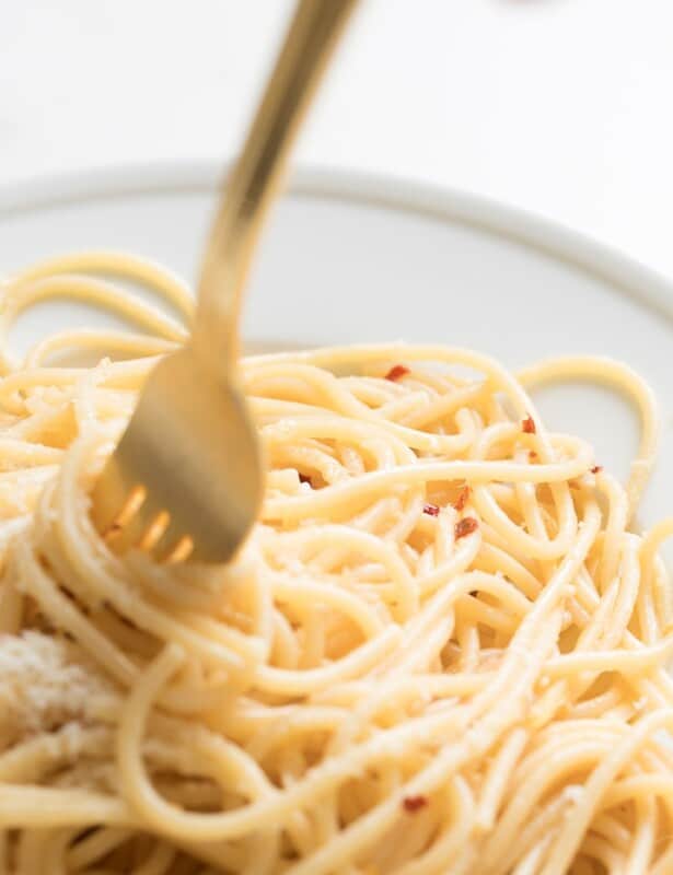 A white plate full of pasta with a gold fork sticking out.
