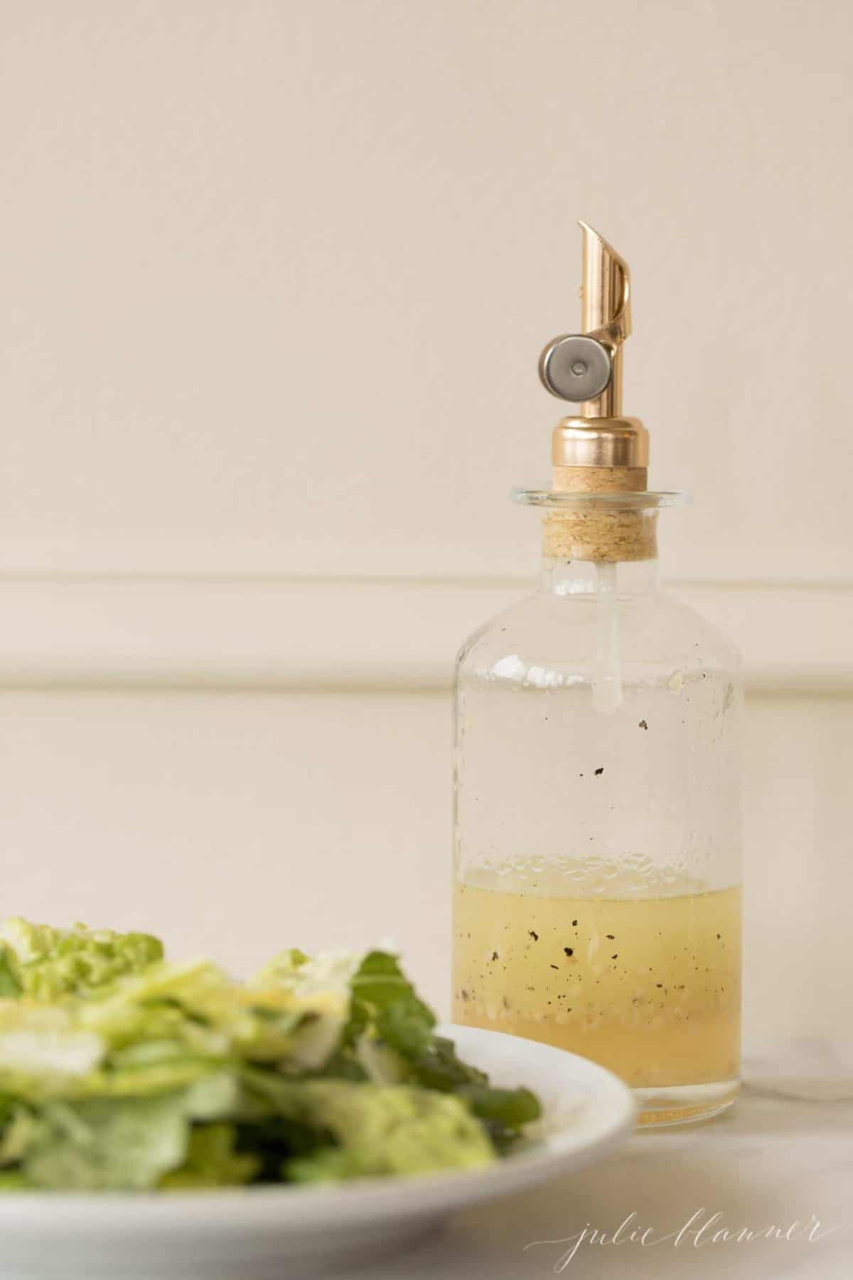 A glass jar of homemade vinaigrette with a salad plate in front.