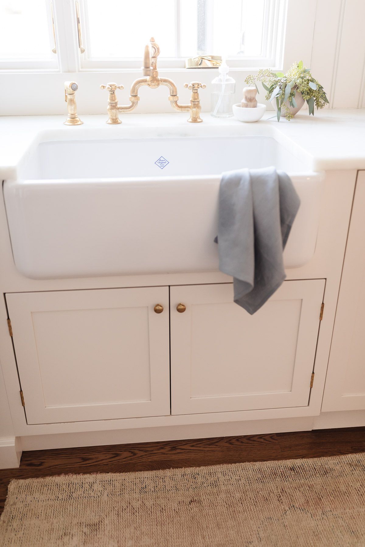 A white farmhouse sink with a brass faucet. 