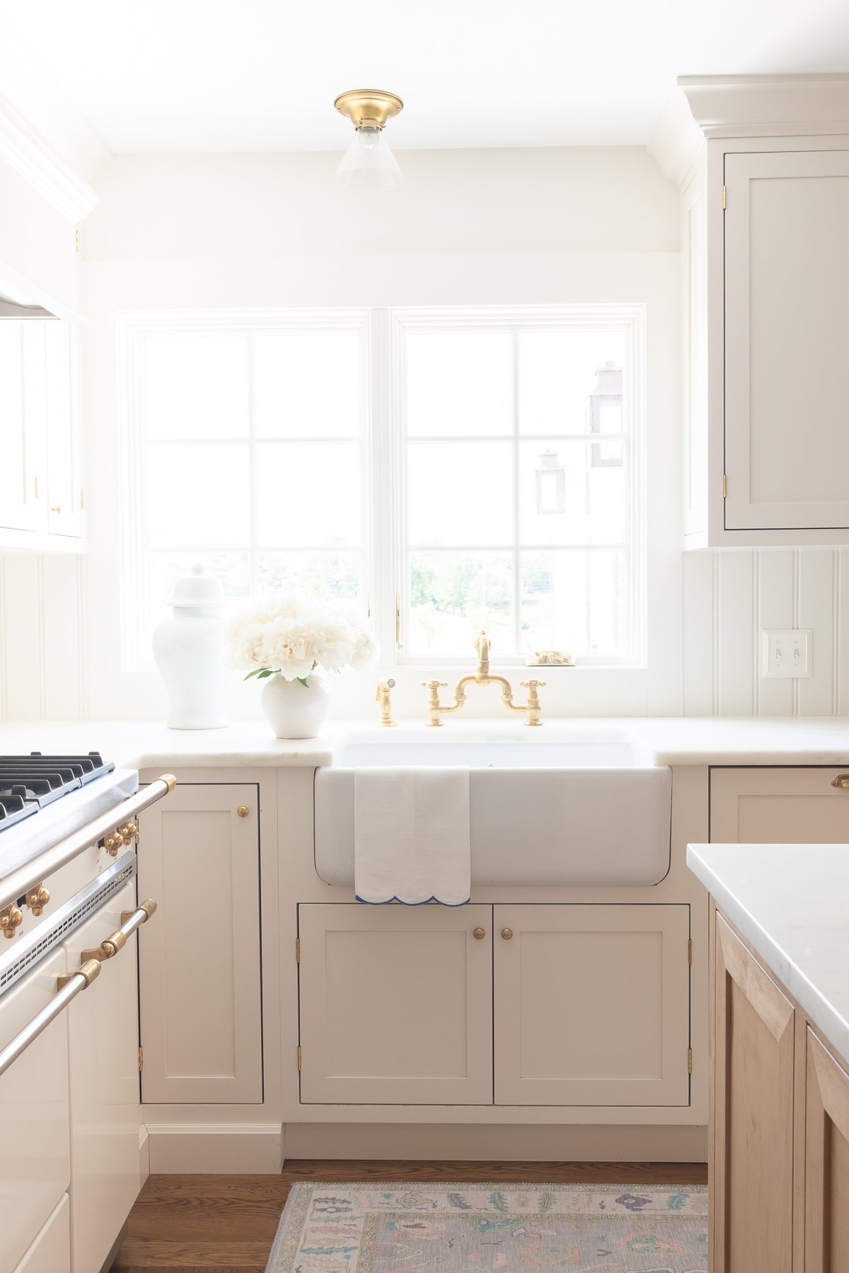 A white kitchen with a farmhouse sink and white flowers. 