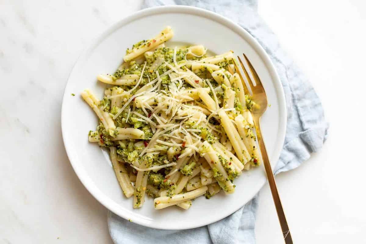 A white plate full of broccoli pasta, gold fork to the side