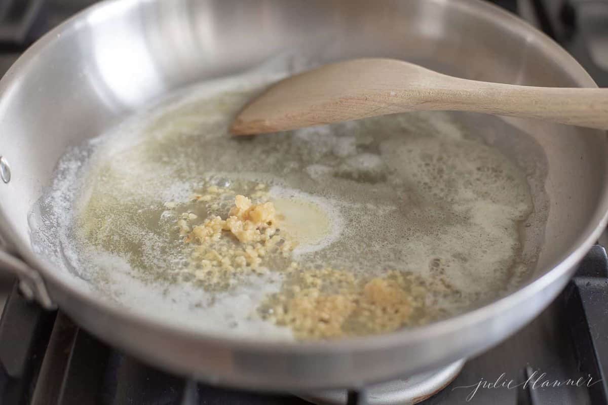 Silver pan on the stove full of butter and minced garlic.