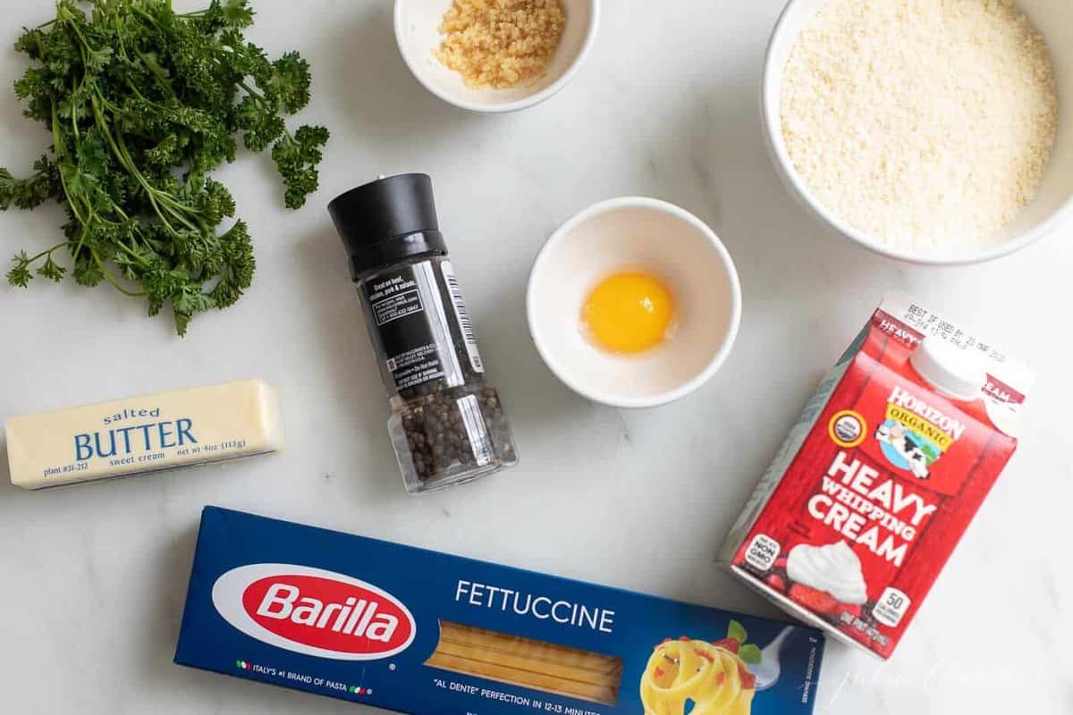 Ingredients for a homemade fettuccine alfredo sauce recipe on a white surface.