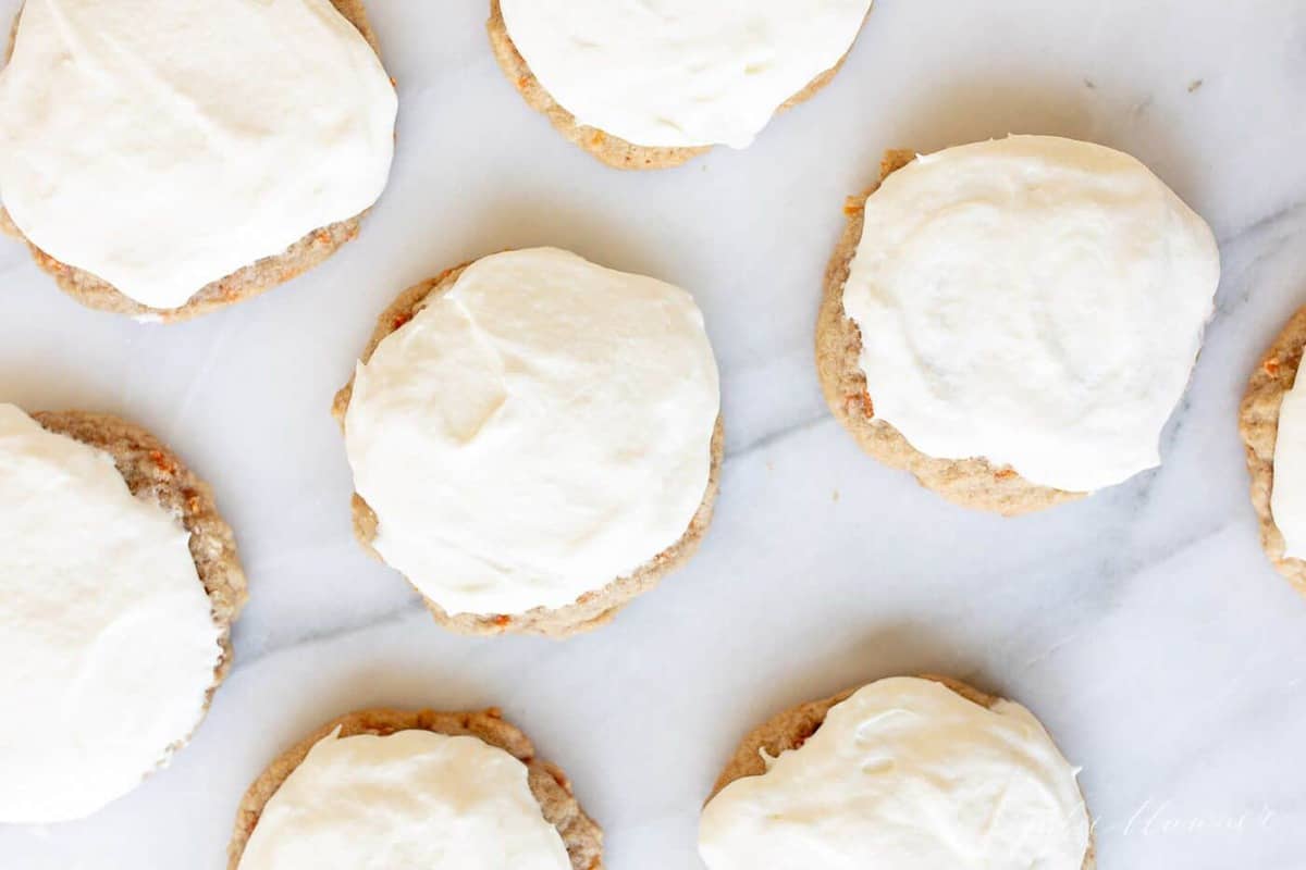 Carrot cake cookies frosted with cream cheese frosting on a marble surface. 