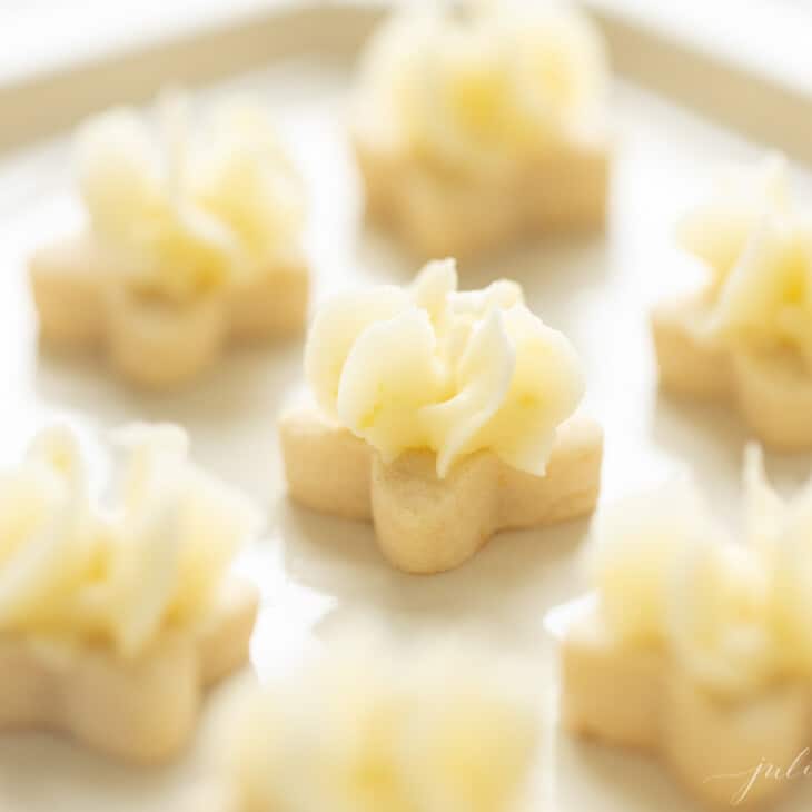 Tiny flower shaped lemon frosted cookies on a white platter.