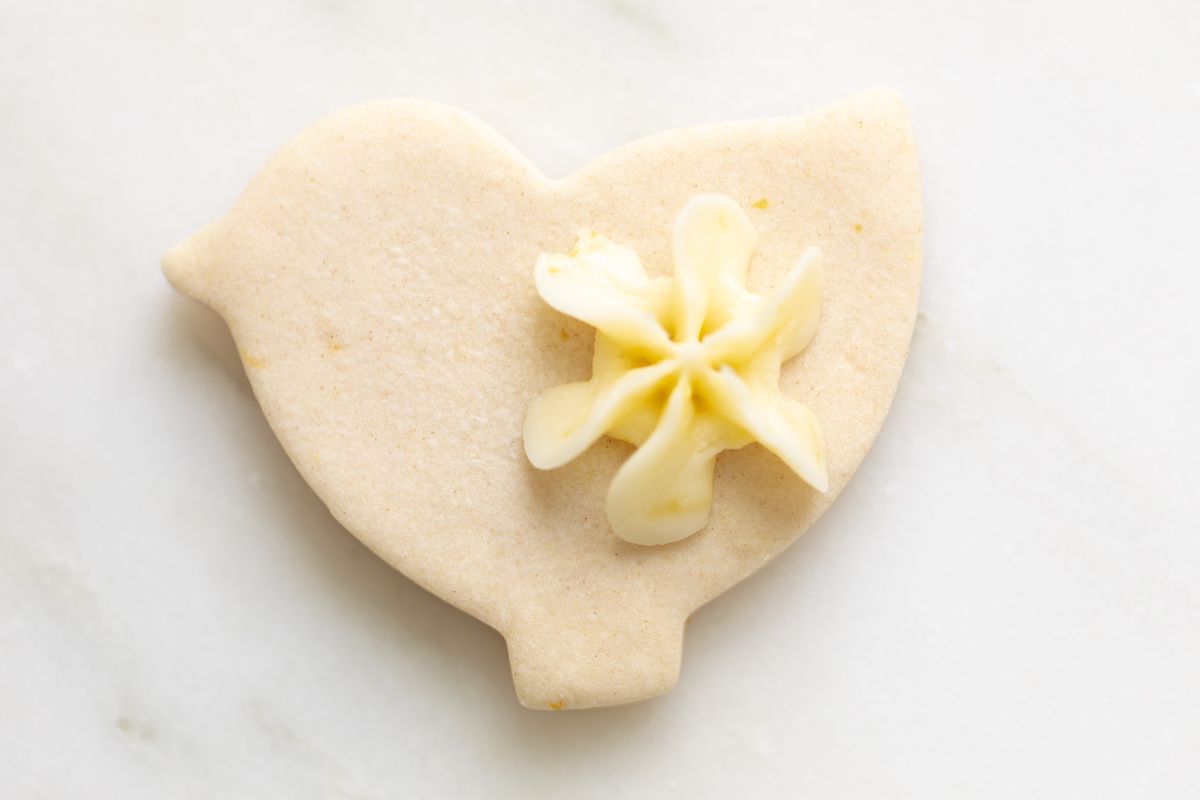 A bird shaped cutout frosted lemon shortbread cookie on a marble countertop.
