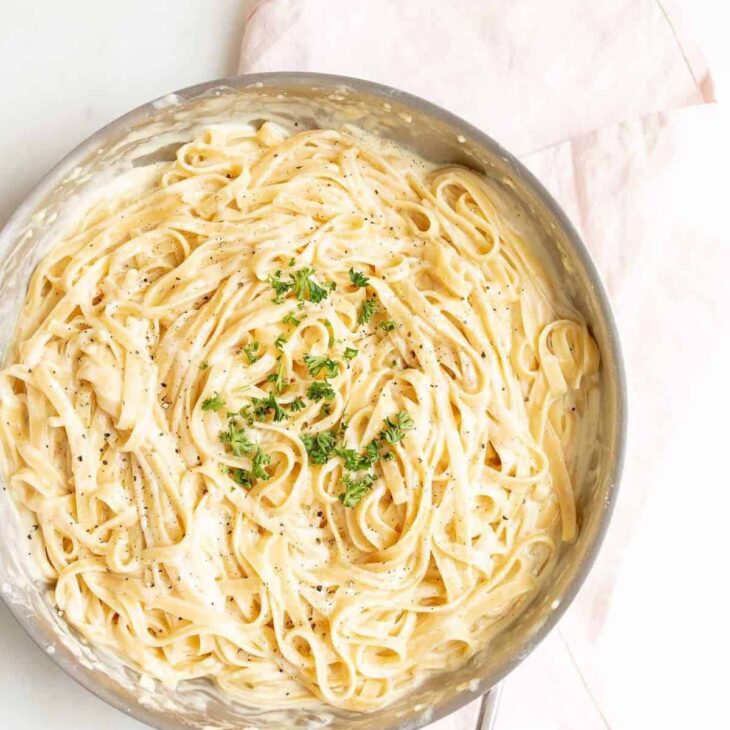 White surface with a metal pan full of homemade fettuccine alfredo.