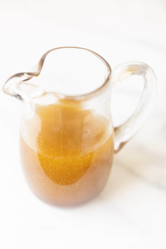 Balsamic vinaigrette in a clear pitcher on a marble surface. 