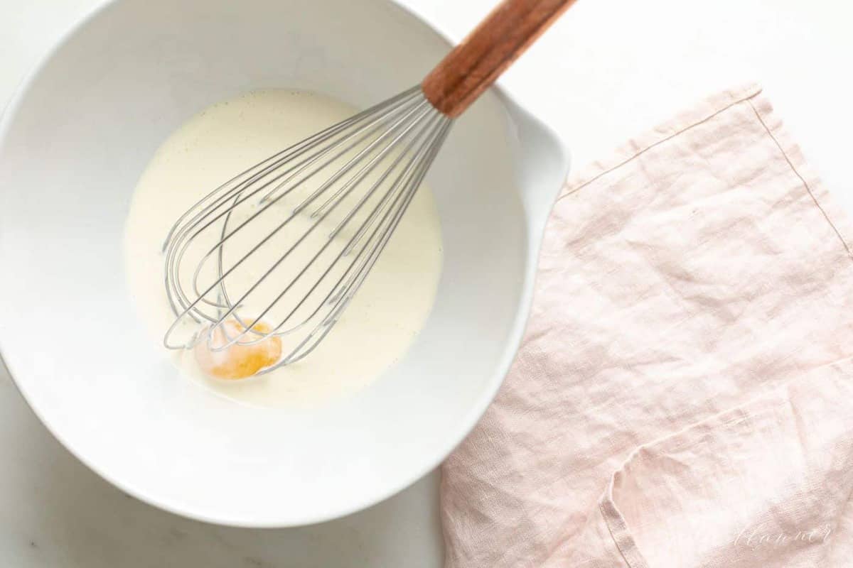 A white bowl full of whipping cream and an egg yolk.
