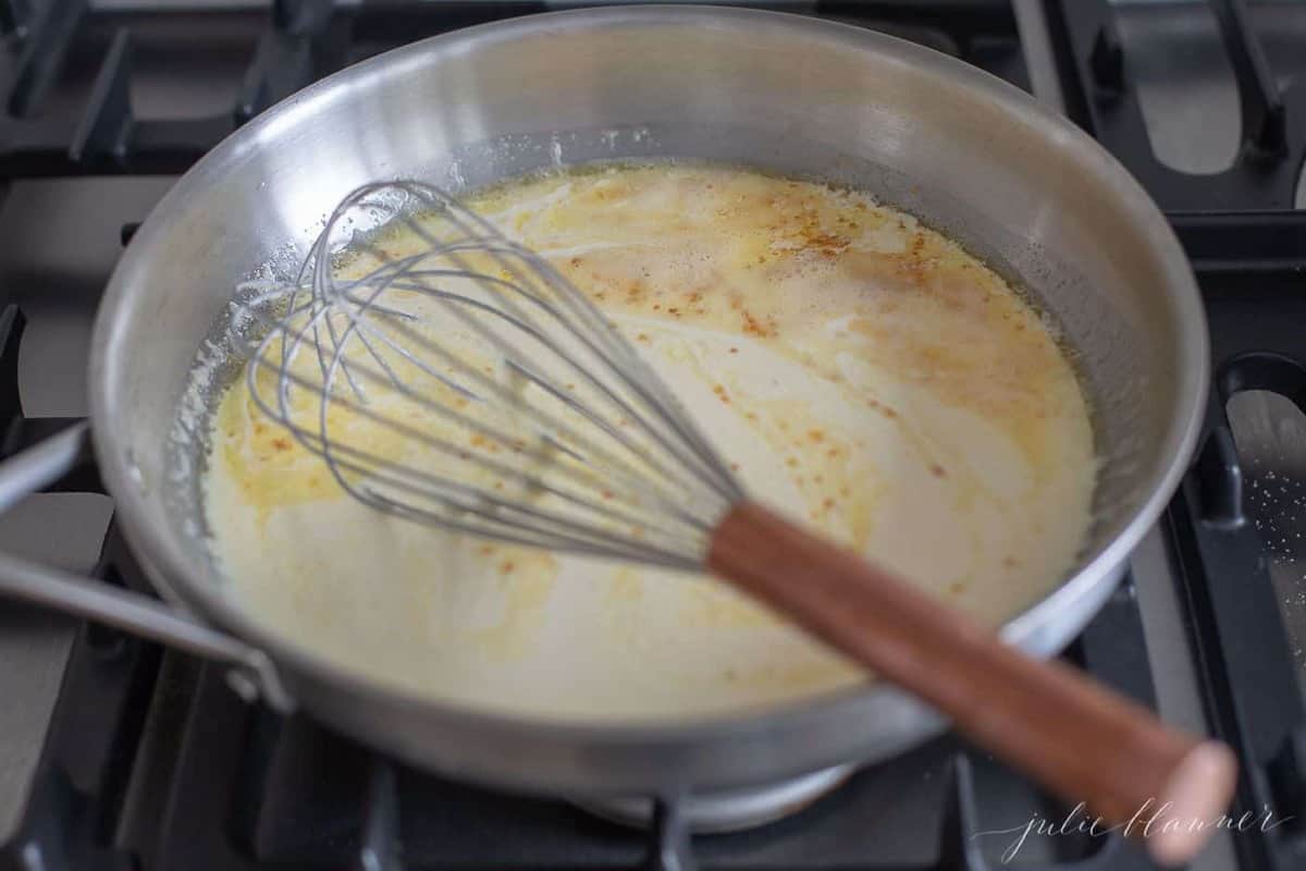 Pan of homemade alfredo sauce on the stove with a whisk to the side.