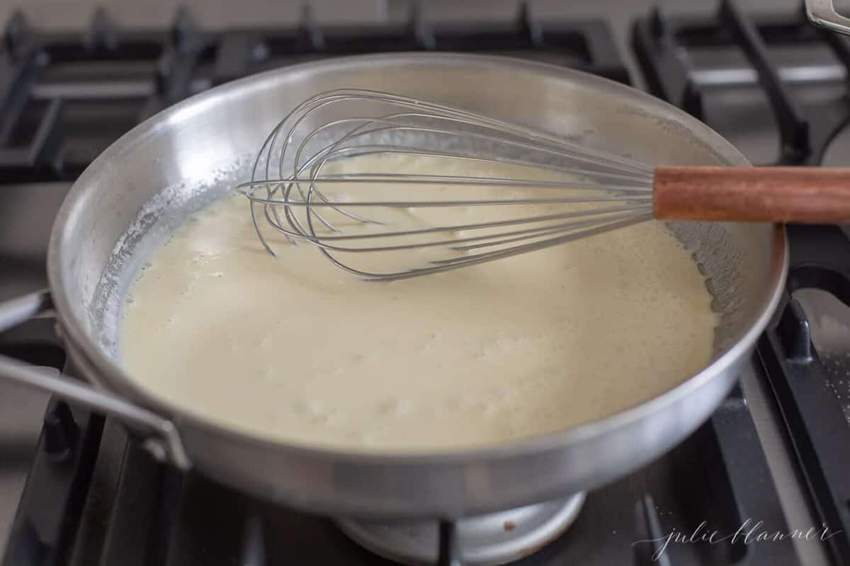 Pan of homemade alfredo sauce on the stove with a whisk to the side.
