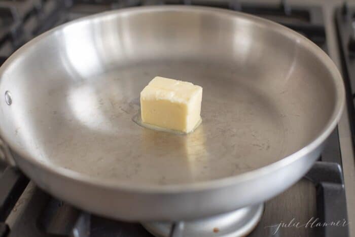 Silver pan on a stove, with a pat of butter.