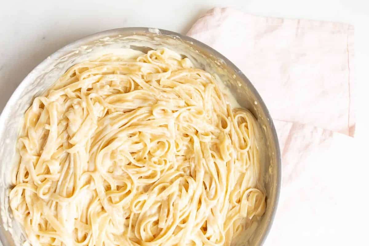 Fettuccine Alfredo in a metal pan on with a pink linen napkin to the side.