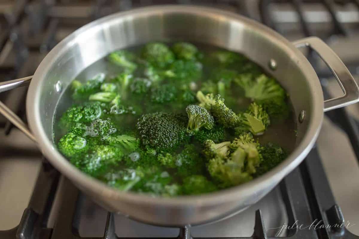a pot on a stove top filled with water and broccoli