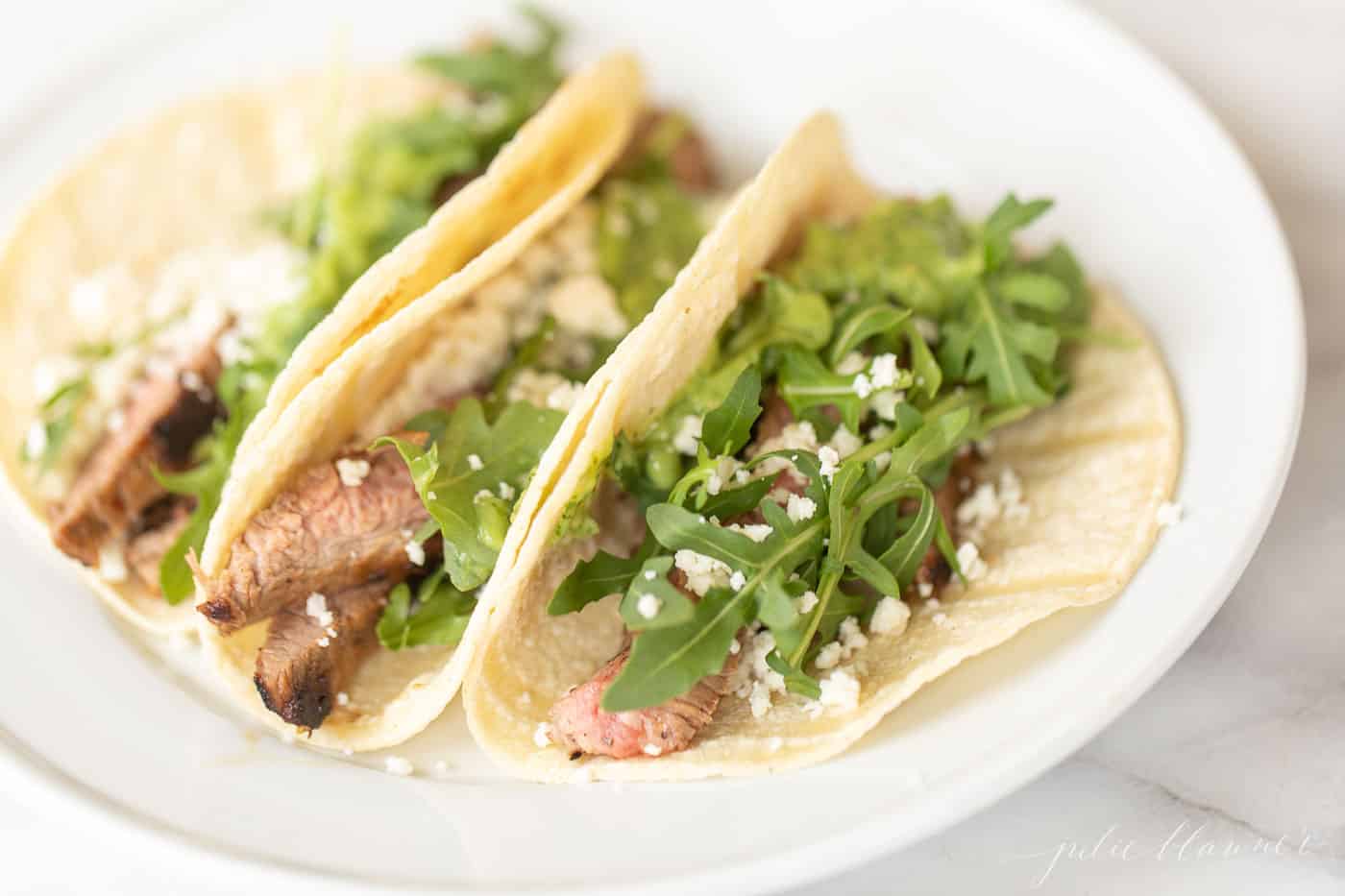 A white plate filled with three carne asada tacos.