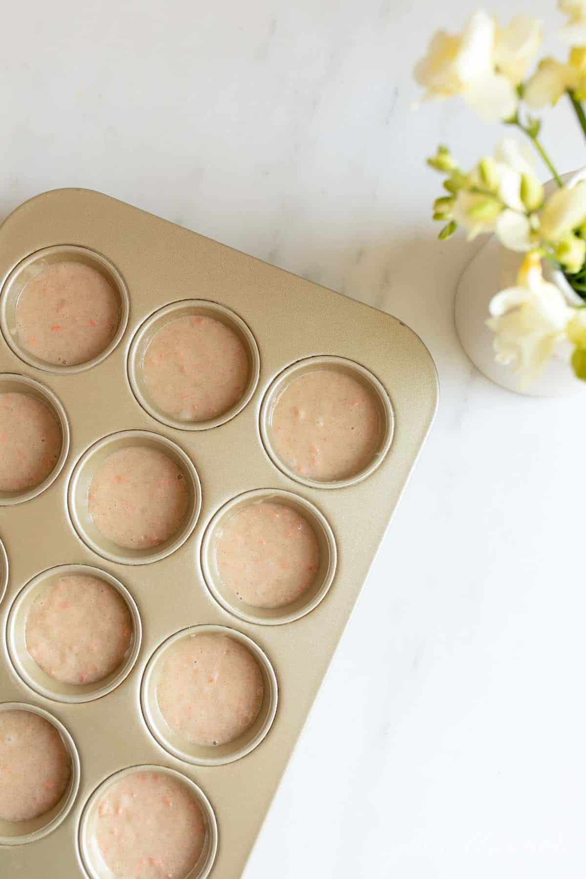 A gold muffin pan filled with carrot cake muffin batter.