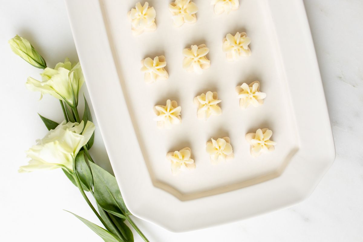 Tiny frosted lemon shortbread cookies on a white platter.