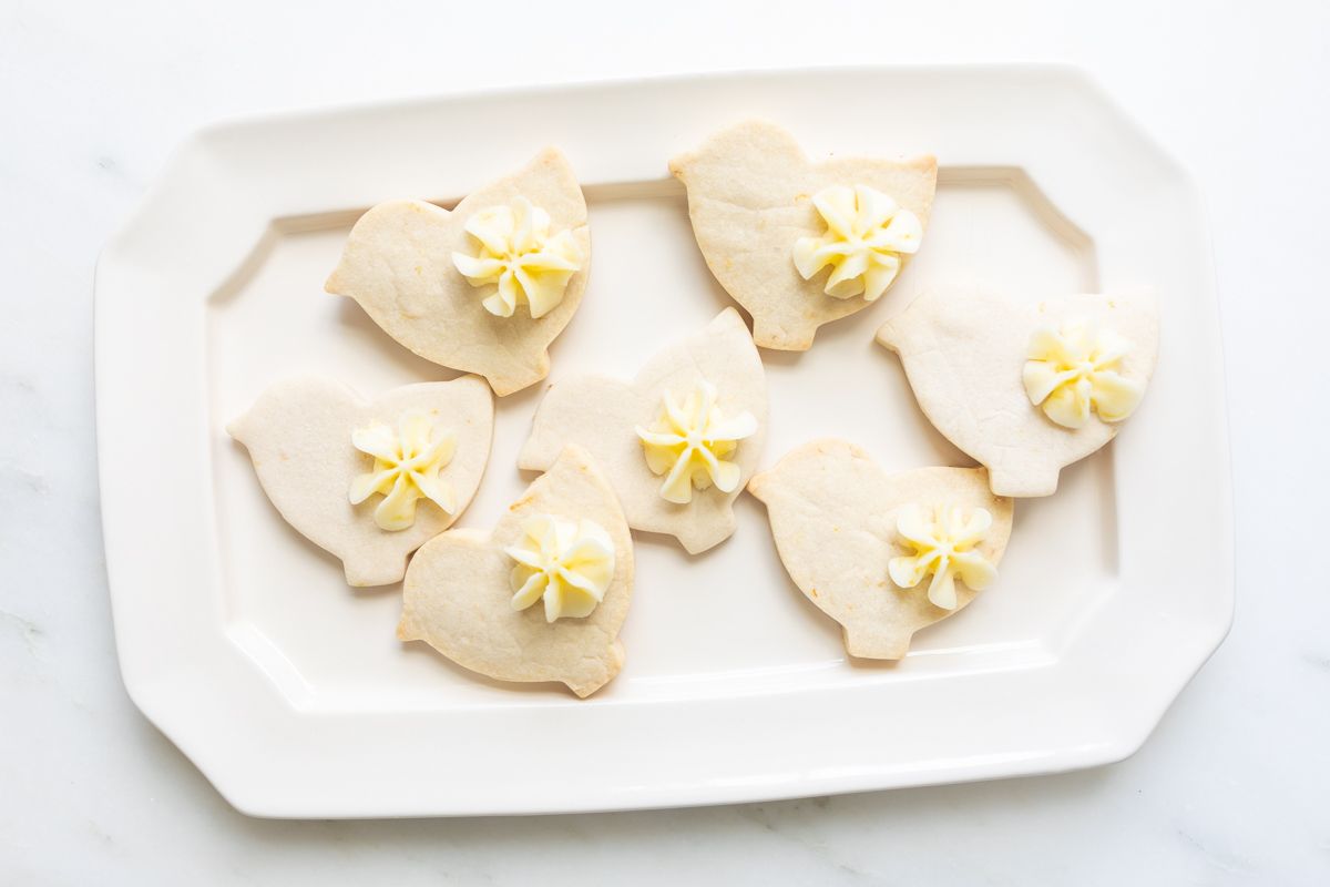 Frosted lemon cookies in a bird shape on a white platter.