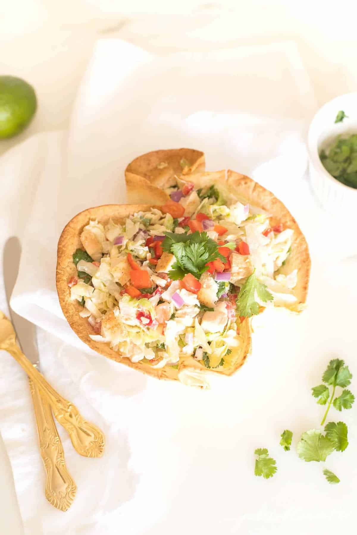 A taco salad served in a tortilla bowl, silverware to the side.