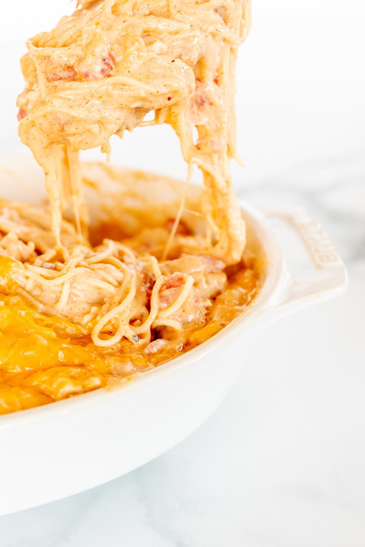 Mexican spaghetti in an oval baking dish, topped with shredded cheese, a scoop being pulled out with a spoon.