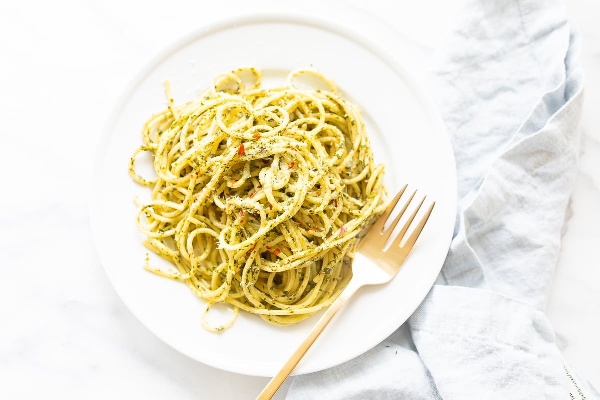 A delicious serving of pesto pasta beautifully presented on a white plate, accompanied by a fork.
