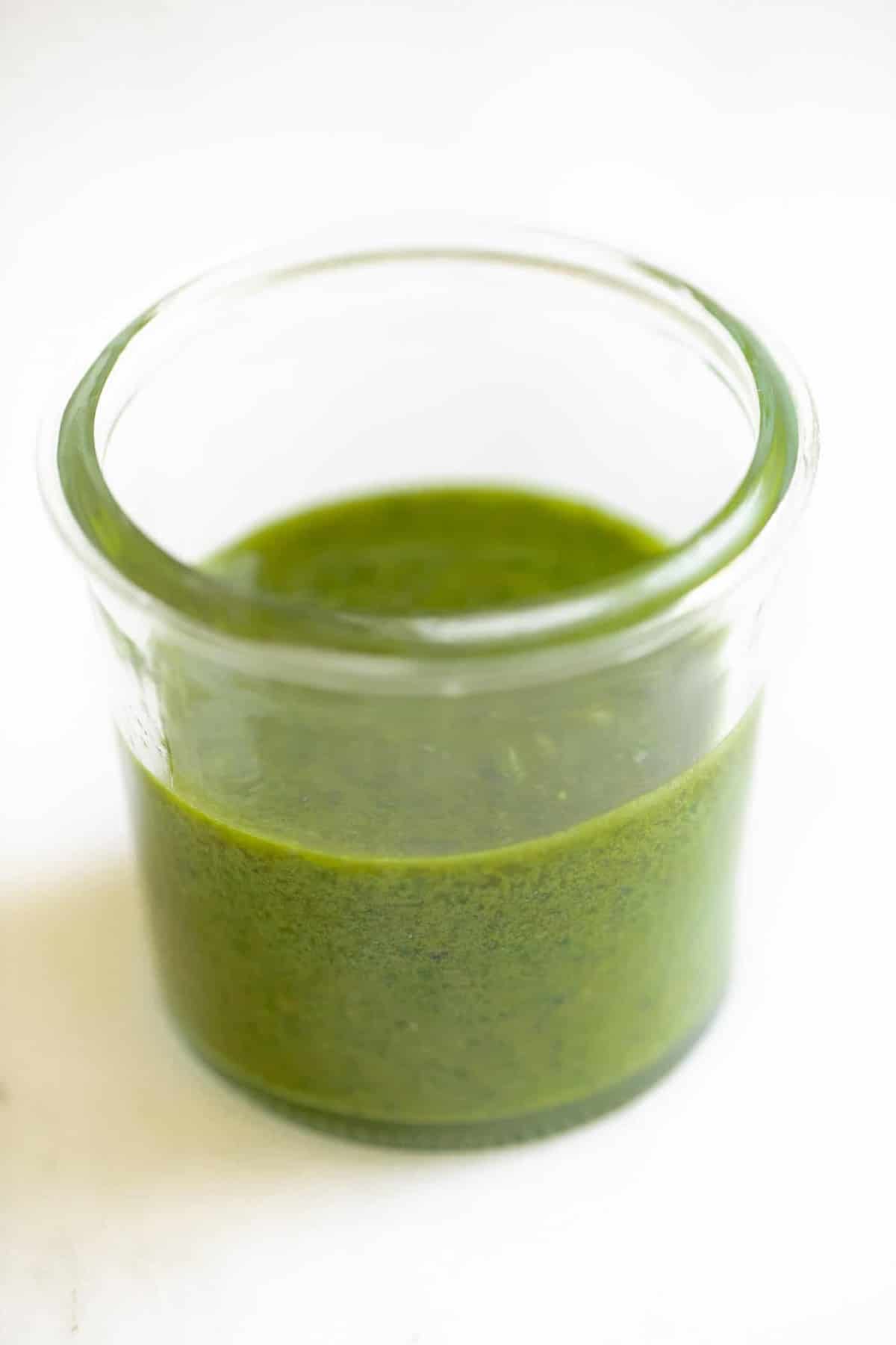 Marble surface with a small clear jar of homemade basil pesto recipe.
