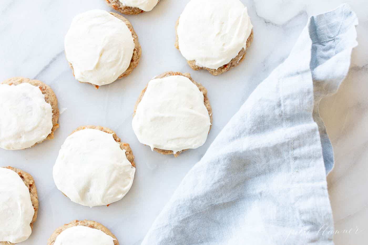 Frosted carrot cake cookies on a marble surface, blue linen towel to the side.