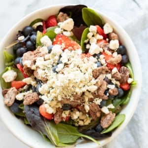 A fresh spring salad with berries, crumbled cheese and nuts in a bowl with wooden serving utensils.
