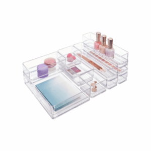 Clear acrylic organizer with various compartments acts as convenient drawer organizers, holding makeup, nail polish bottles, pencils, small jars, and notebooks—all neatly arranged on a white background.