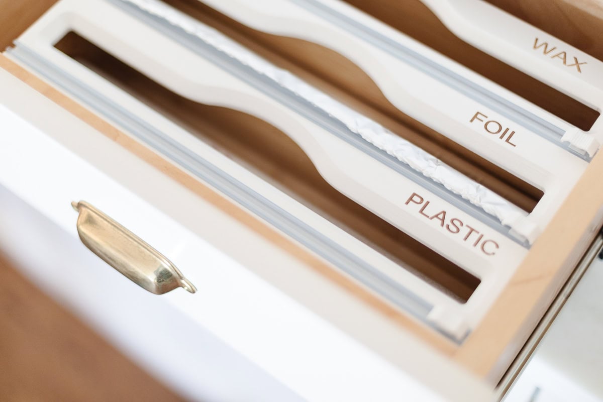An organized kitchen drawer features labeled compartments and built-in cutters for wax paper, foil, and plastic wrap, enhanced by convenient drawer dividers.