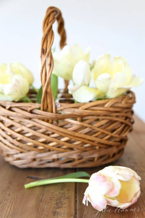 A wicker basket with a white dish inside, yellow tulips placed at the beginning of a flower basket arrangement.