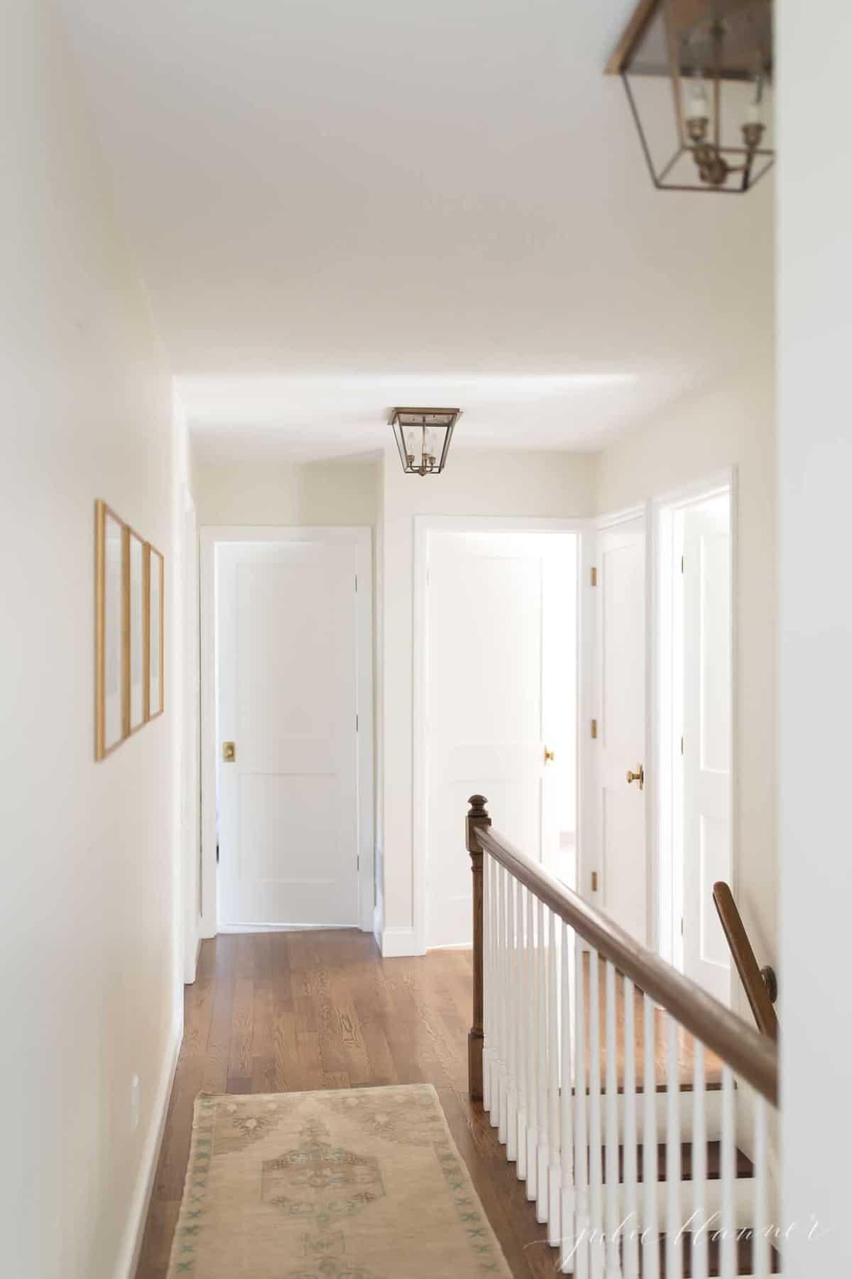A white upstairs hallway in a home with a Kilim rug on the floor.
