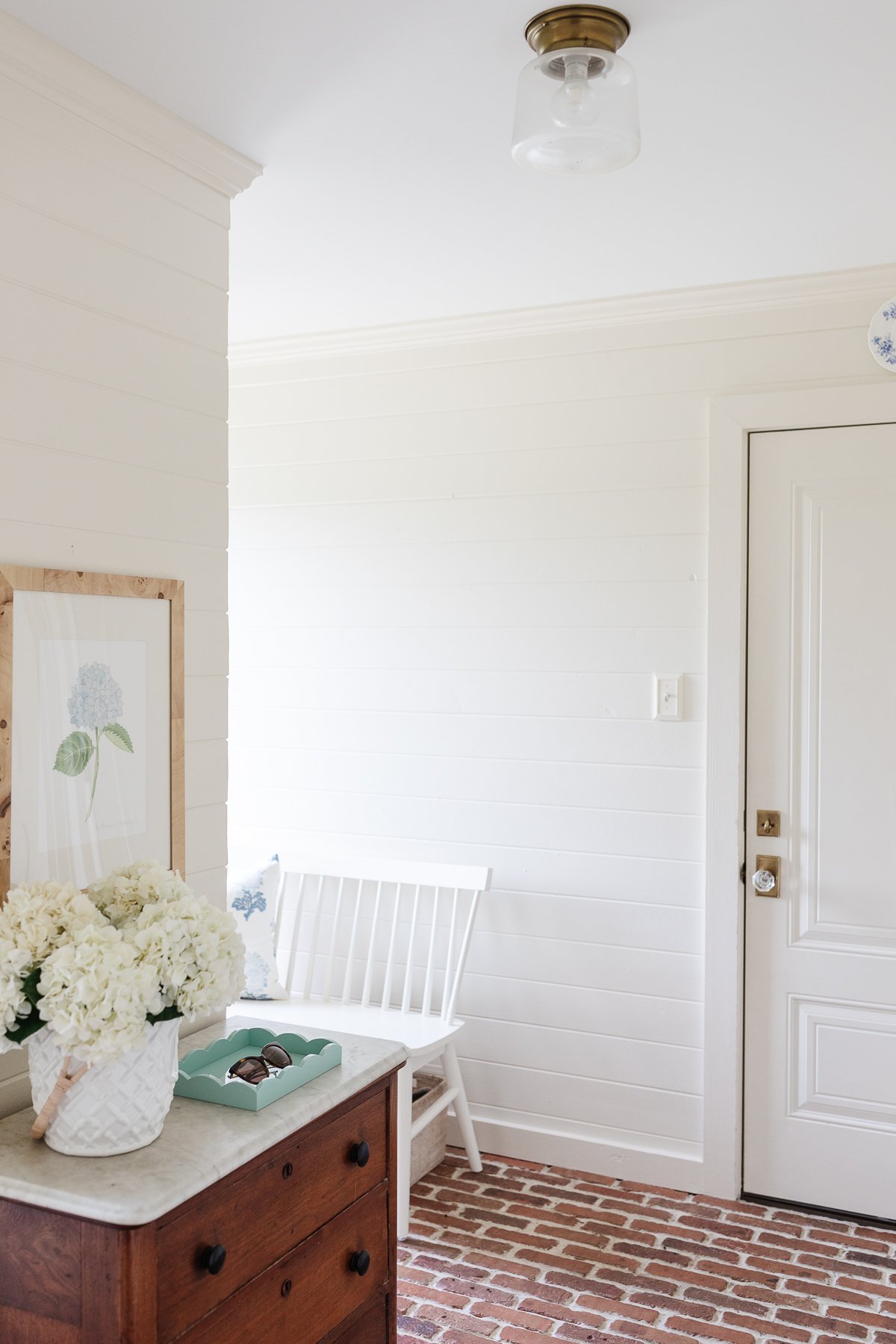 A mudroom with white paneled walls and brick floors