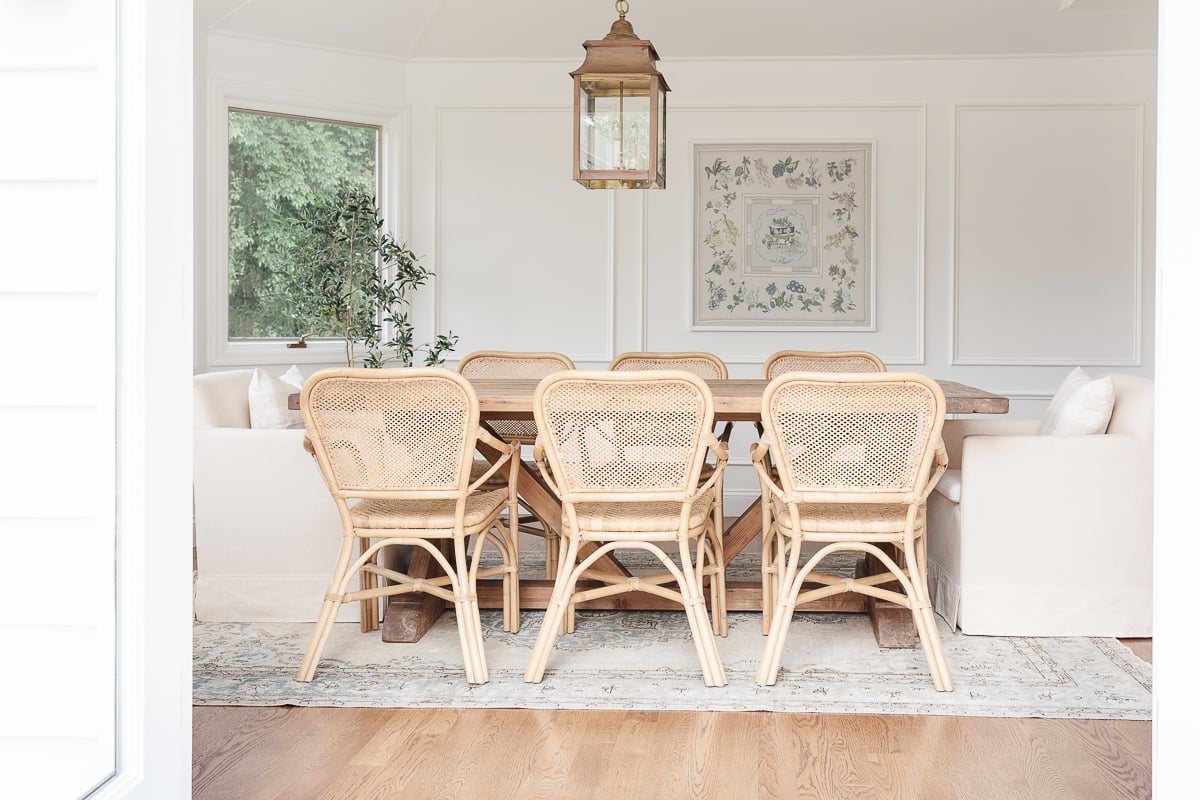 A white dining room space with moulding on the walls and a wood farm table. 