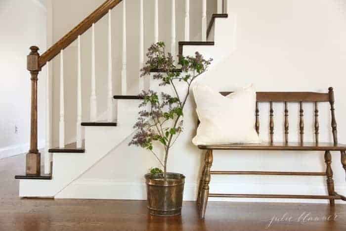 An entryway with white walls, a wooden bench and wooden stairs in a home with character.