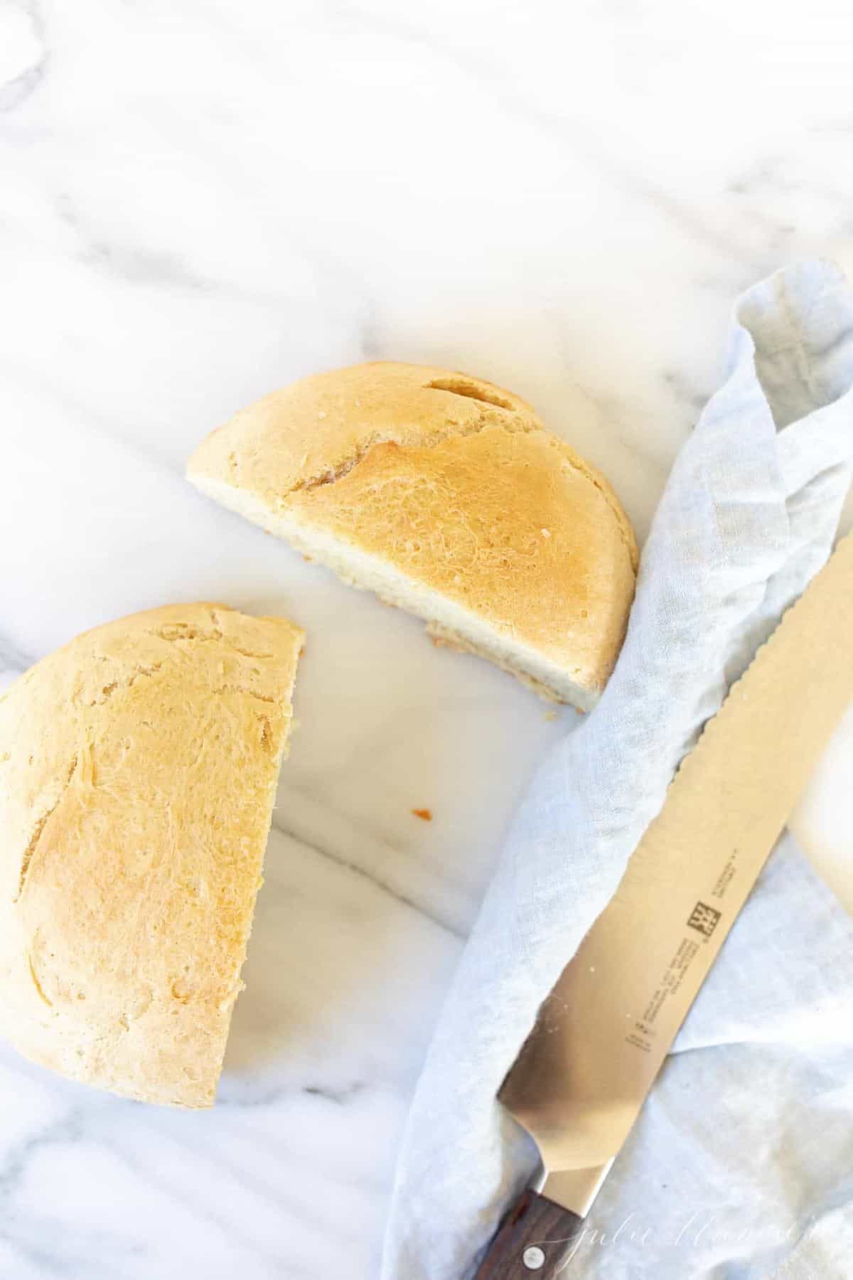 Marble surface with a loaf of homemade rosemary olive oil bread, knife to the side.