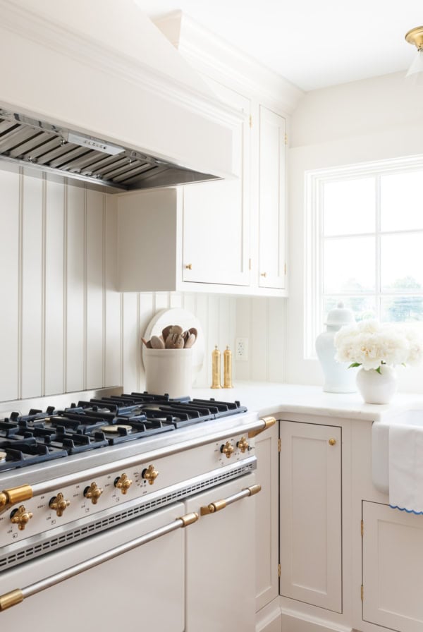 Elegant white kitchen with a gas stove, white marble countertops and gold hardware