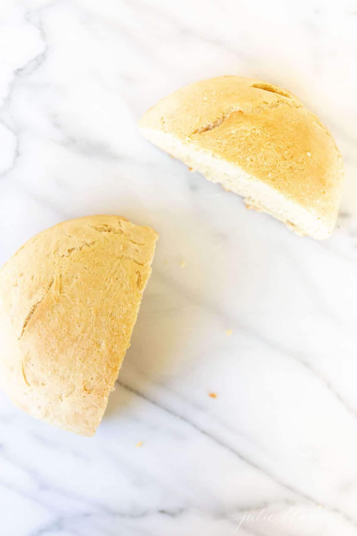 A loaf of round homemade bread baked with yeast, sliced in half on a marble surface.