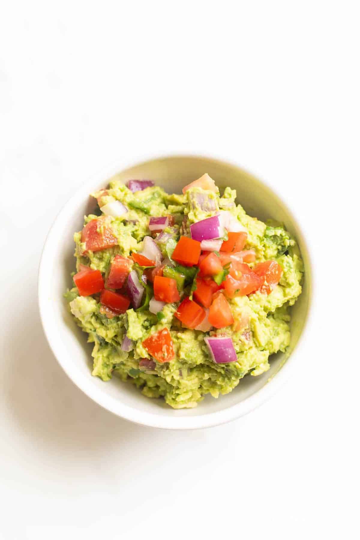 A white bowl on a white surface, filled with a homemade guacamole recipe.