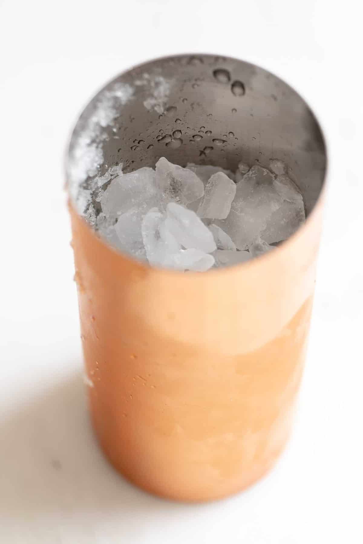 White surface, copper cocktail shaker filled with ice.