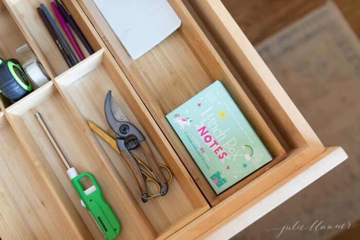 A junk drawer opened with a wooden organizer, filled with home items and essentials.